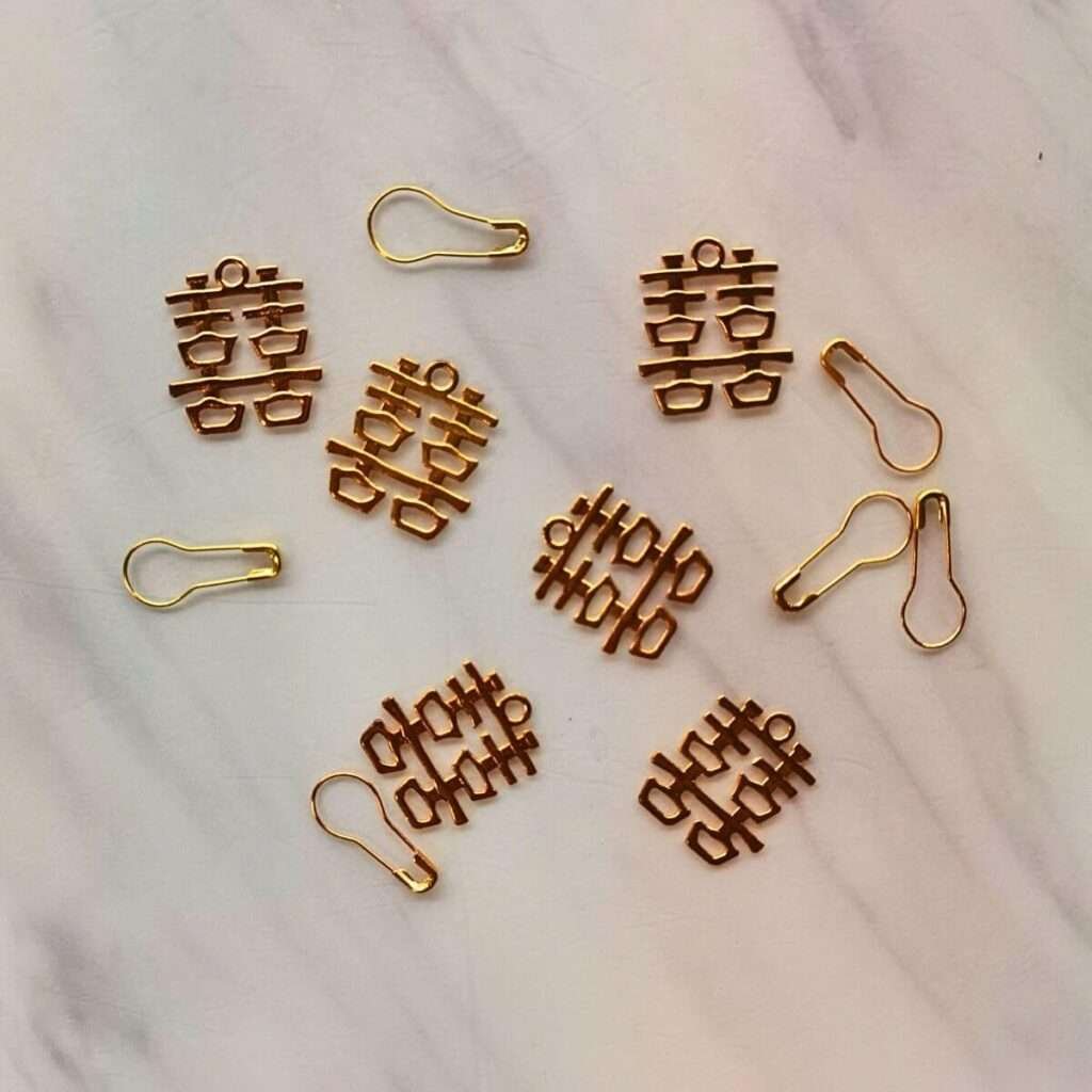 Golden double happiness symbols paired with pear-shaped paperclips on a white marble background.