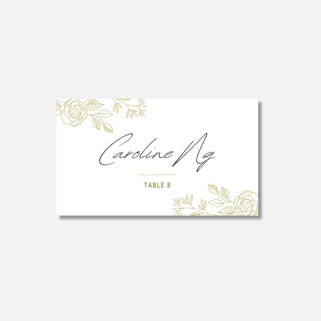 Elegant white guest name tag from the Premium Package with golden floral designs, displaying 'Caroline Ng' and 'Table 8'.