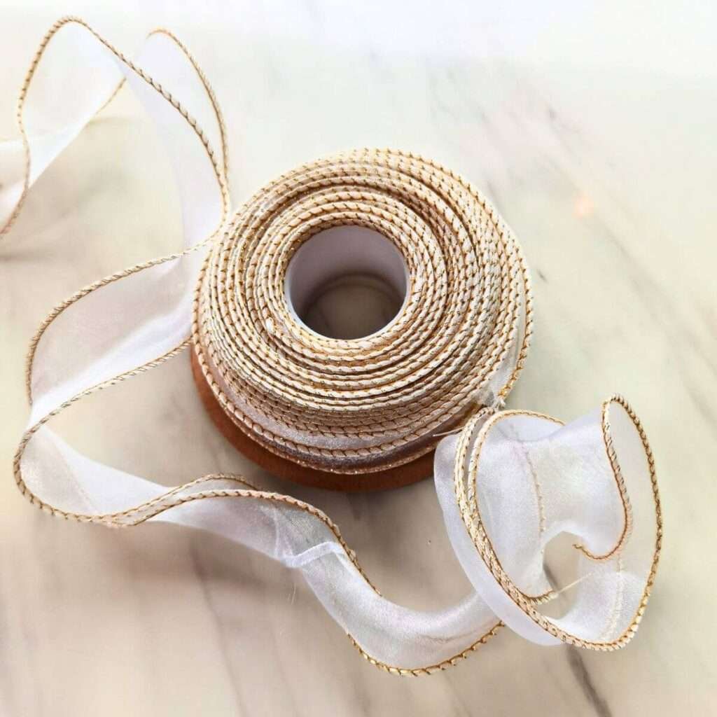 Rolled sheer organza ribbon with delicate gold trim, displayed on a white marble surface with loose tendrils unfurling.