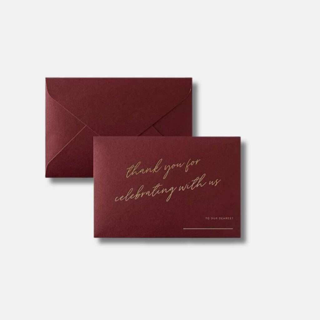 Premium 'Thank You For Celebrating With Us' invitation envelope in wine red with gold text and a designated space for guest names at the bottom right corner.